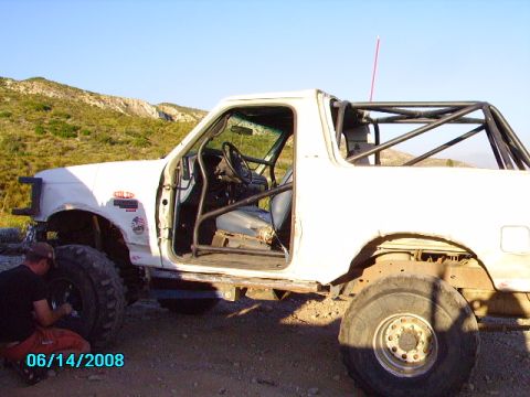 1990 Ford Bronco - This 1990 Ford Bronco has been modified with a roll cage and is seen outdoors with a person working on its front wheel.