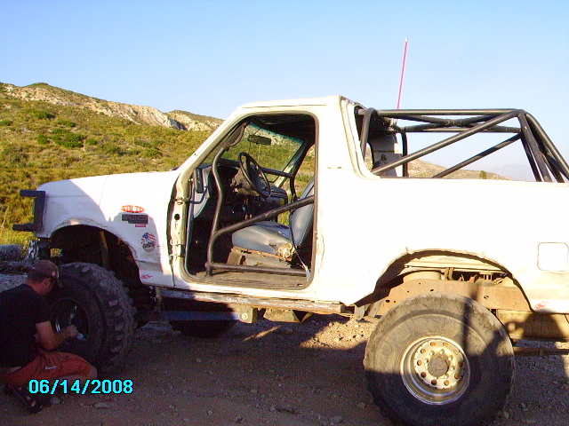 1990 Ford Bronco with roll cage, doors removed, and a person working on the front tire