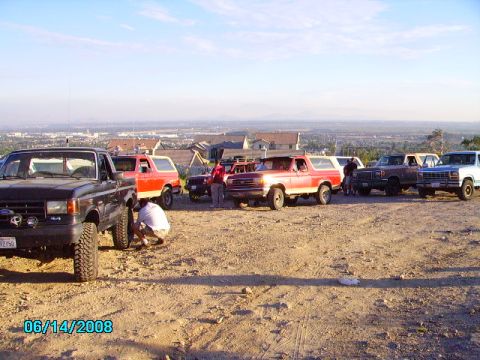1990 Ford Bronco - A group of Ford Broncos and trucks are parked on a hill with a town in the background.