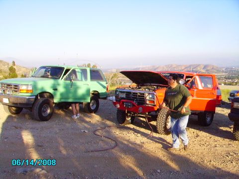1990 Ford Bronco - Two Ford Broncos are parked on a dirt lot with a person working on one of them.