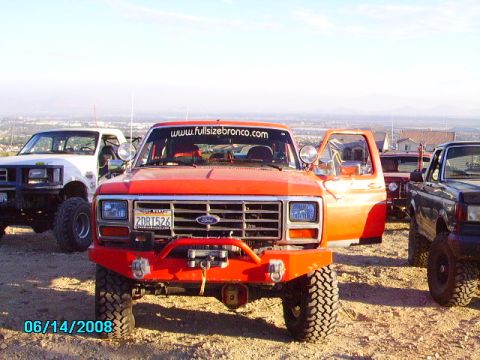 1990 Ford Bronco - Multiple off-road vehicles are parked on a dusty hill with a city in the background.