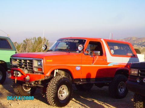 1990 Ford Bronco - This modified orange Bronco features off-road tires and a distinctive white stripe along its side.