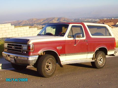 1990 Ford Bronco - Side view of a red and white 1990 Ford Bronco parked outdoors.