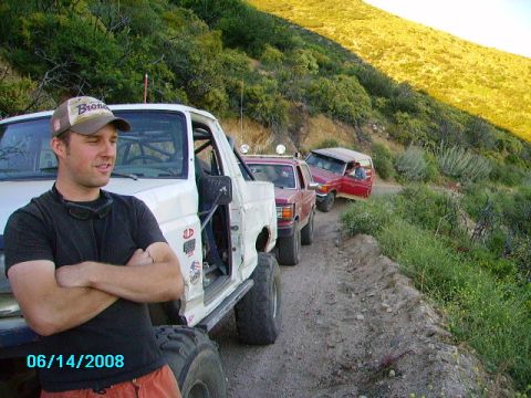 1990 Ford Bronco - A convoy of modified Broncos navigates a dusty trail on a sunny day.