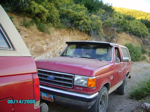 1990 Ford Bronco - Two vehicles are parked on a dirt road with brush and hills in the background.