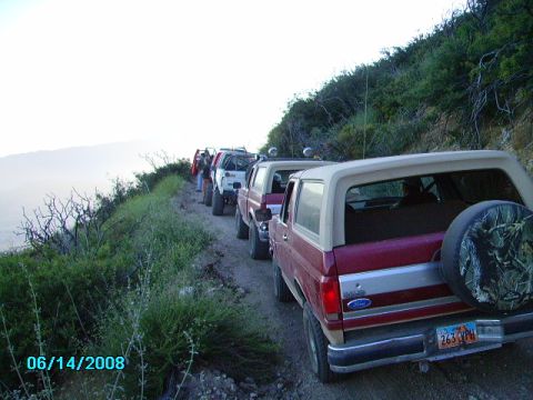 1990 Ford Bronco - A line of Ford Broncos drives down a dusty mountain road.