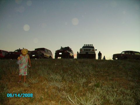 1990 Ford Bronco - A group of off-road vehicles are gathered on a hill as the sun sets, with a child in the foreground.