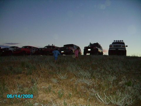 1990 Ford Bronco - A group of SUVs and trucks are parked on a grassy hill under a twilight sky, with two children in the foreground.