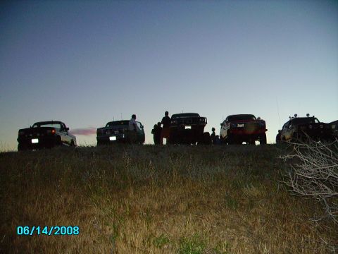 1990 Ford Bronco - Several SUVs, including a 1990 Ford Bronco, are parked on a grassy hill under a twilight sky.