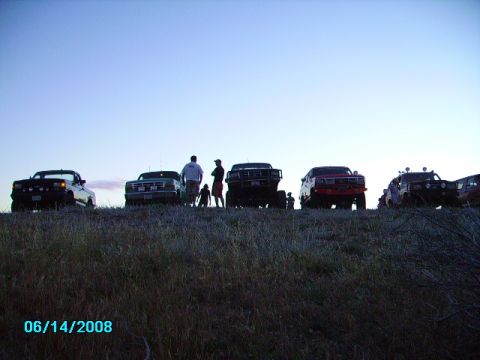 1990 Ford Bronco - Multiple SUVs are parked on a grassy hill under a clear sky at dusk.