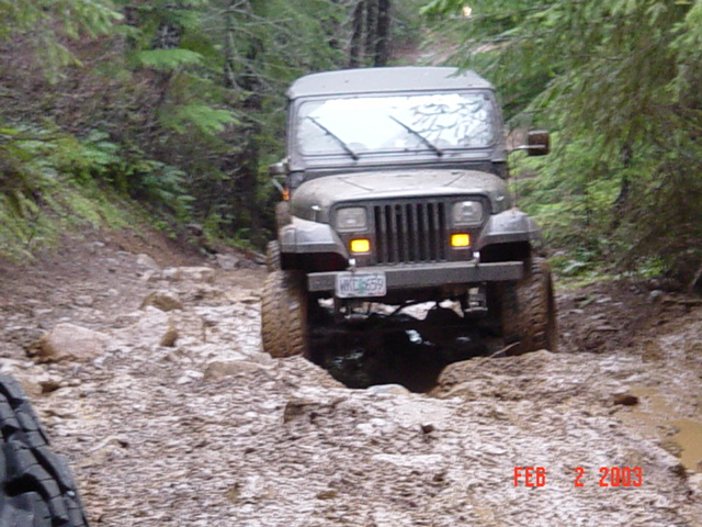1995 Jeep Wrangler navigating a rough, rocky, and muddy forest trail