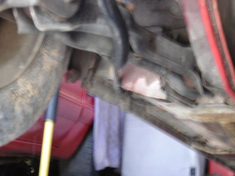 1988 Ford Bronco - Close-up view of the undercarriage of a red vehicle, with visible suspension parts and a tool.