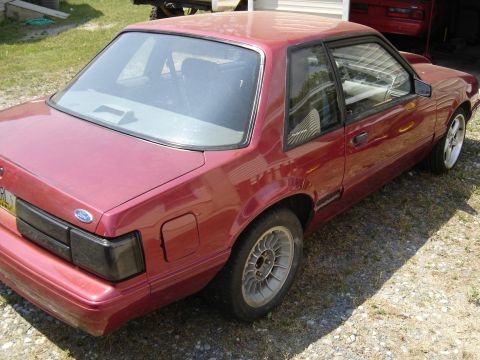 1988 Ford Bronco - A red Ford Mustang coupe is parked outside, with another red vehicle visible in the background.
