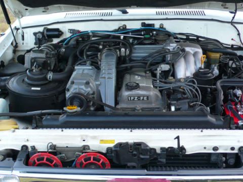 1986 Ford Bronco - The engine bay of a vehicle, the 1FZ-FE engine and two red horns visible below the radiator.