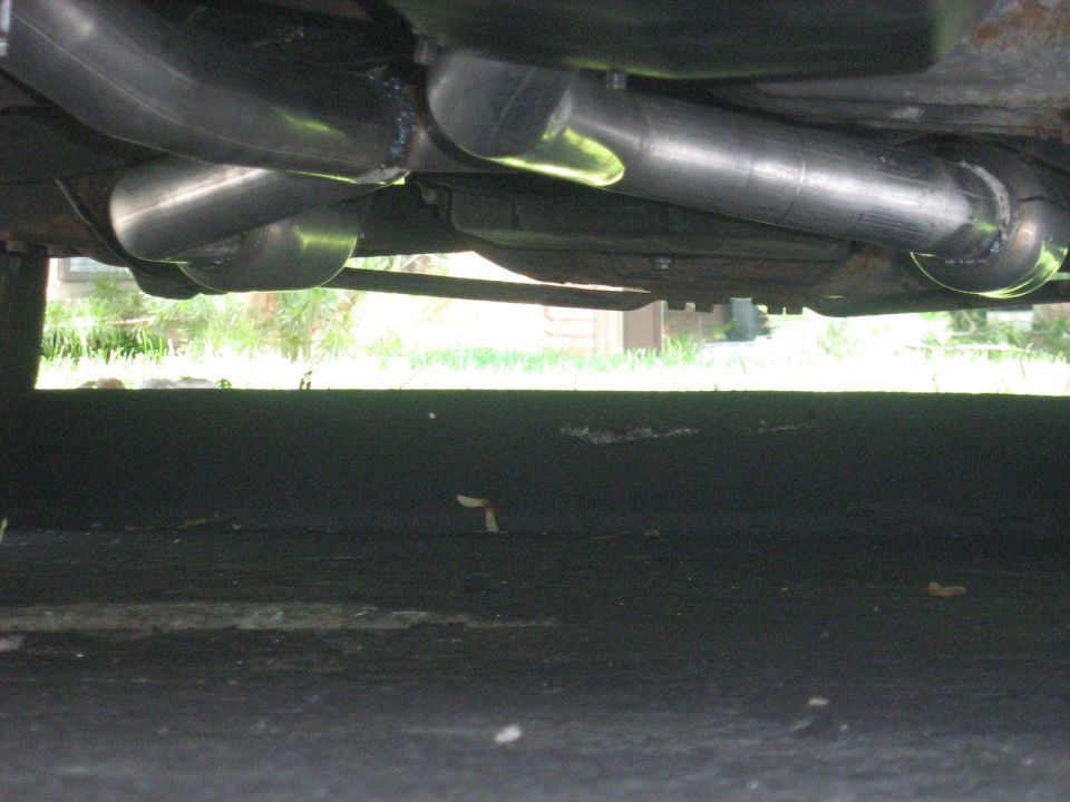 Underside of a car showing dual exhaust mufflers over grass