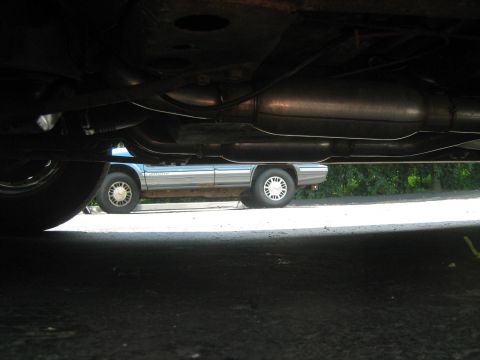 1988 Mercury Grand Marquis - A silver sedan is visible beneath the undercarriage of another vehicle, suggesting a late 1980s model.