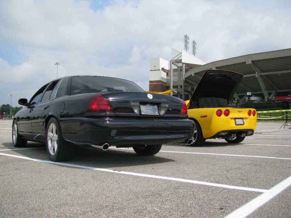 Black Mercury Marauder parked next to a yellow Chevrolet Corvette with its trunk open