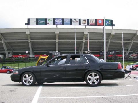 2003 Mercury Marauder - A black sedan is parked in front of a stadium with various sponsor logos visible on the upper facade.