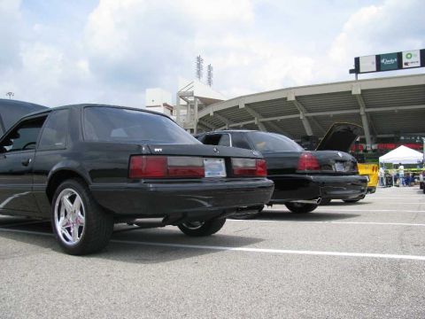 2003 Mercury Marauder - Two black sedans, one a 1993 Ford Mustang SVT Cobra, are parked at a car show with stadium seating in the background.