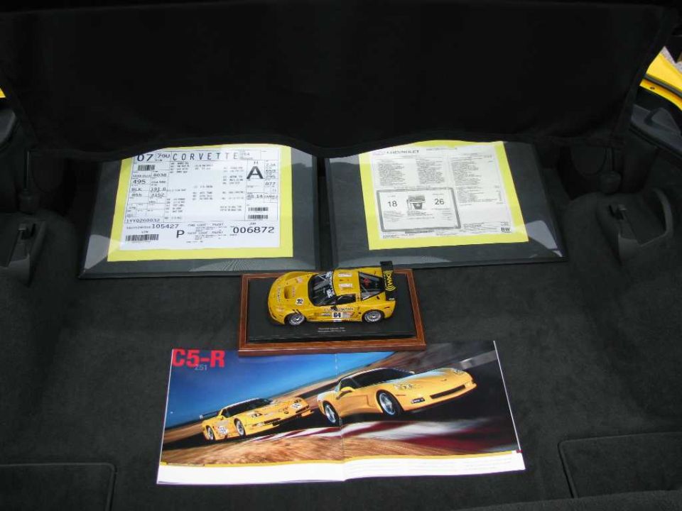 Two yellow window stickers and a yellow 2007 Corvette model car sit in a car's trunk