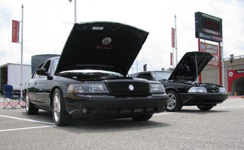 2003 Mercury Marauder - Two black sedans with hoods open are parked at an outdoor event, with a stadium scoreboard in the background.