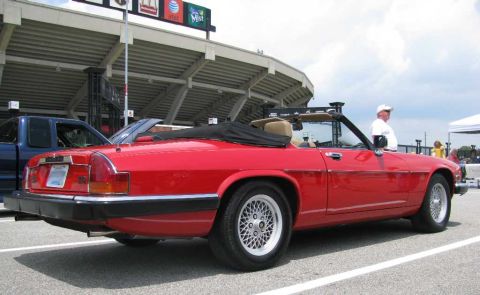 2003 Mercury Marauder - A red convertible Jaguar is parked in a lot with a blue pickup truck nearby, under a stadium structure.