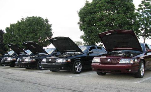 2003 Mercury Marauder - A line of Mercury Grand Marquis sedans, hoods raised, parked in a lot with trees in the background.