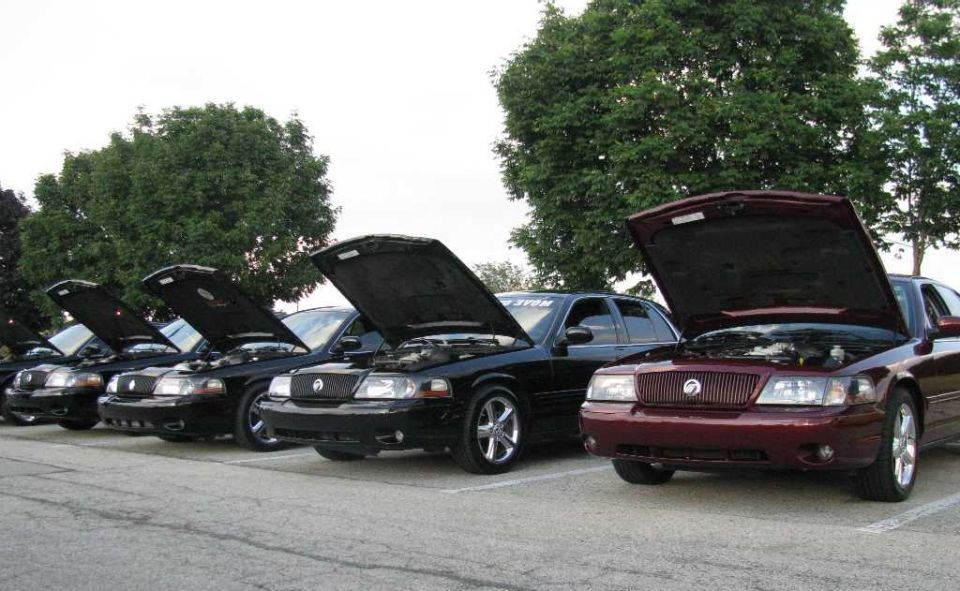 Several Mercury Grand Marquis sedans lined up with hoods open. One is maroon, the rest are black