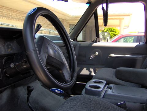 1987 Ford Bronco - The interior of a 1987 Ford Bronco shows a Ford-branded steering wheel cover and a floor-mounted gear shifter.