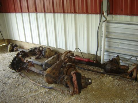 1992 Ford Bronco - Two rusty axles, likely from a truck or SUV, lie on the ground next to a red hydraulic cylinder.