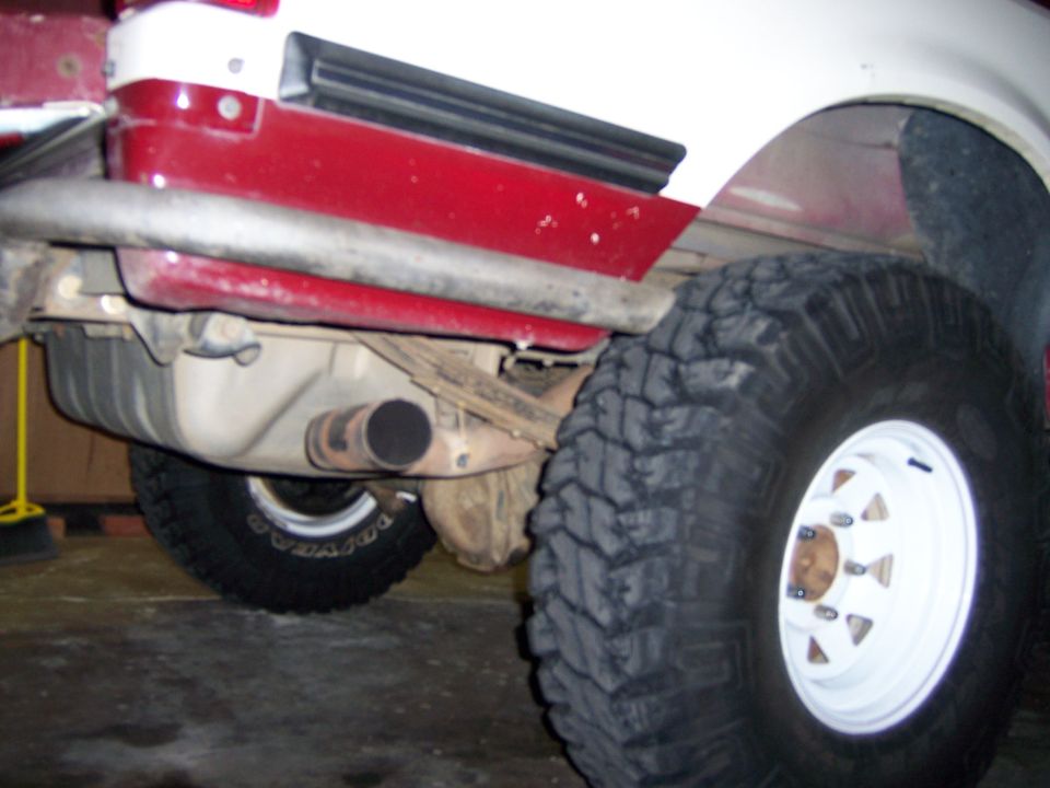 Rear axle, fuel tank, and exhaust pipe visible under a truck with large off-road tires