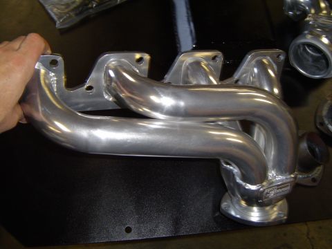 1978 Ford Bronco - A polished exhaust manifold is held by a hand, with a brand name visible on the flange.