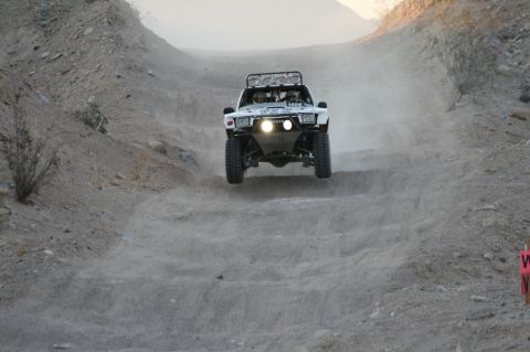 1996 Ford Bronco - A modified Toyota truck navigates a dusty off-road course, catching air over a rough section.