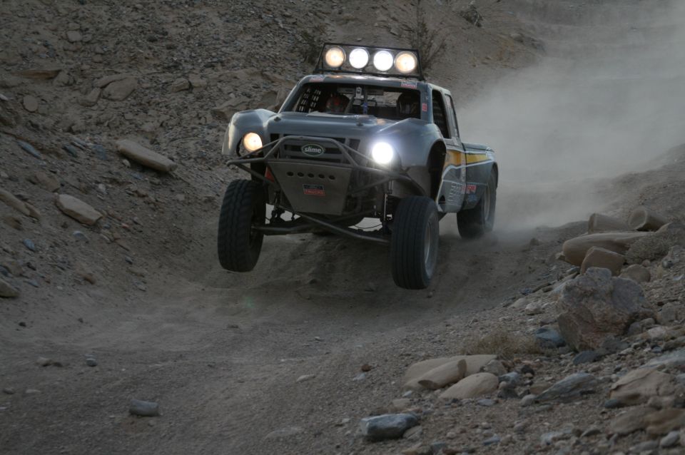 Off-road truck kicking up dust while jumping over a rocky trail