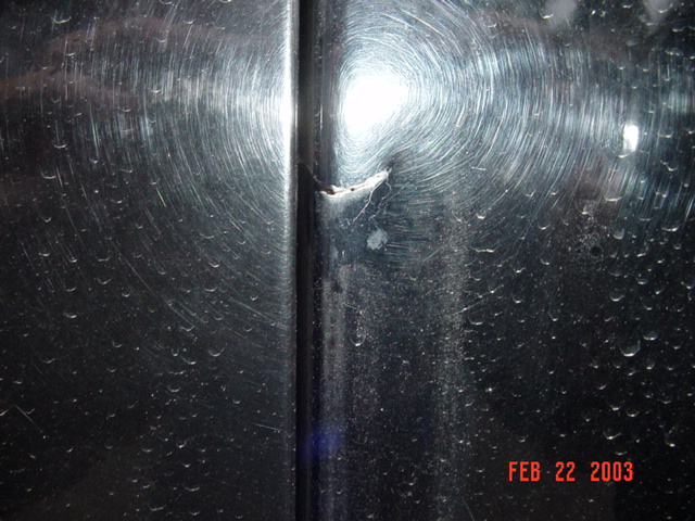 Close-up of cracked black B-pillar trim with water spots on a dark vehicle body