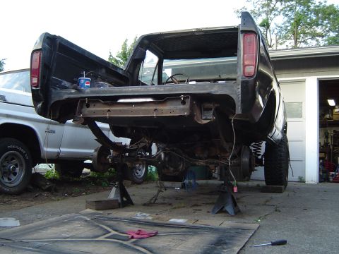 1979 Ford Bronco - The rear of a black truck is disassembled and elevated on jack stands, with a silver truck parked nearby.