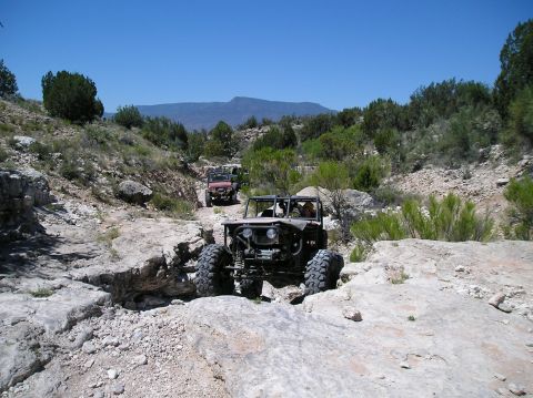1986 Toyota Hilux - Multiple off-road vehicles traverse a challenging rocky terrain under a clear blue sky.