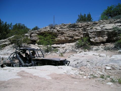 1986 Toyota Hilux - A heavily damaged off-road vehicle sits abandoned in a dry, rocky terrain under a clear blue sky.
