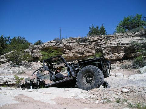 1986 Toyota Hilux - This heavily modified off-road vehicle navigates a challenging rocky landscape under a clear blue sky.