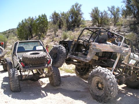 1986 Toyota Hilux - Modified off-road trucks with oversized tires are seen in a challenging outdoor environment.
