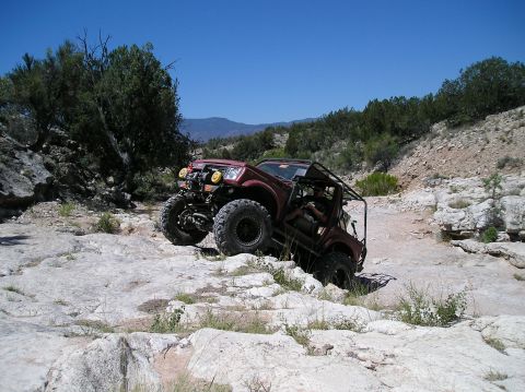 1986 Toyota Hilux - This heavily modified off-road vehicle is shown tackling a challenging rocky terrain.