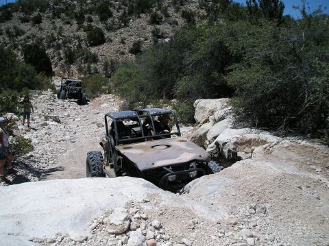 1986 Toyota Hilux - Multiple off-road vehicles traverse a challenging, rocky terrain under a clear sky.