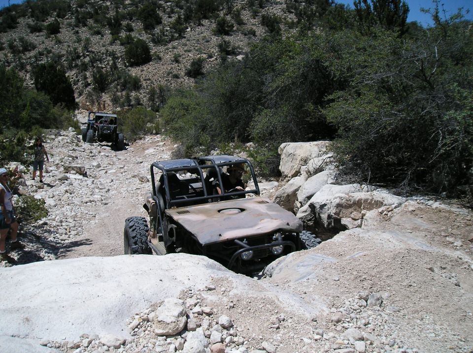 Off-road buggy with a roll cage navigating a rocky trail, front right tire lodged between rocks