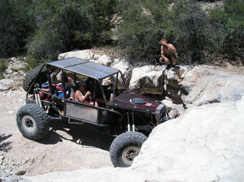 1986 Toyota Hilux - A custom-built off-road buggy is shown navigating a challenging rocky terrain, with a spectator observing from the side.