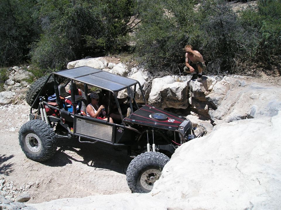 Off-road buggy navigating a rocky trail with people inside and one person watching