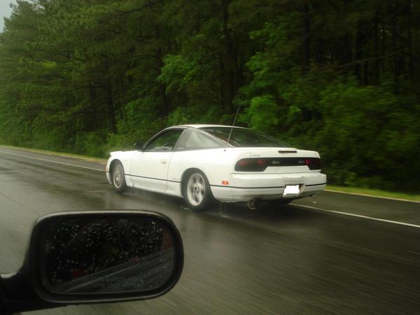 White coupe driving on a wet road, seen from side mirror