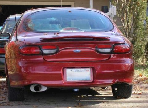 1997 Ford Taurus - The rear of a red sedan is visible, parked in front of a garage with another vehicle to its left.