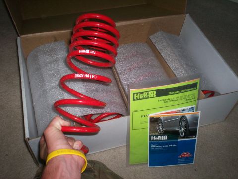 1993 Ford Probe - A person holds a red H&R coil spring, part of a performance suspension kit, with installation guides nearby.