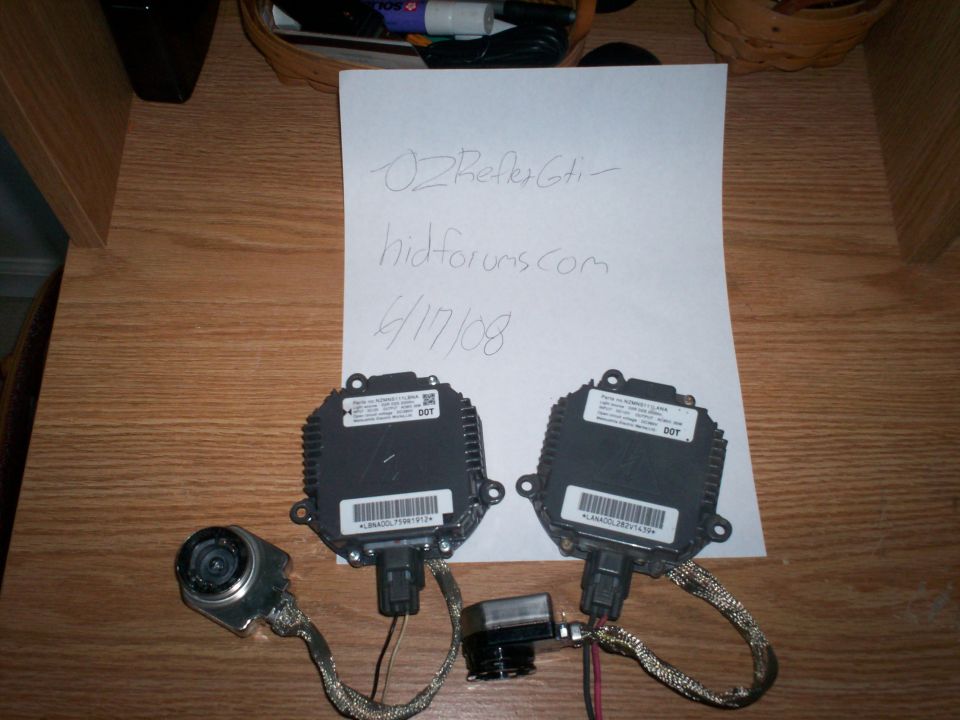 Two black HID ballasts and one igniter on a wooden surface with a handwritten note