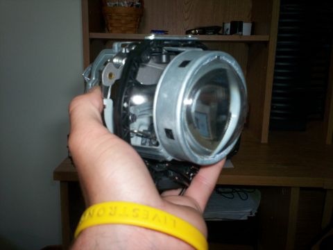 1993 Ford Probe - A person holds a car headlight projector assembly, which is a component of a vehicle's lighting system.